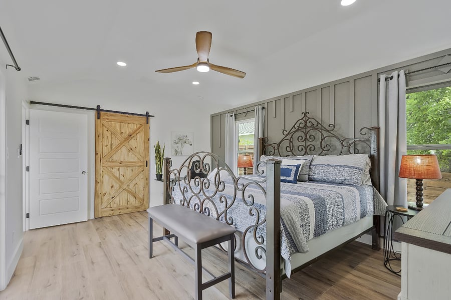 Master bedroom with a king bed, barn door, and large walk-in closet, attached to an ensuite with a large walk-in custom shower with rain head and dual vanities. Large adjustable height desk and office chair.