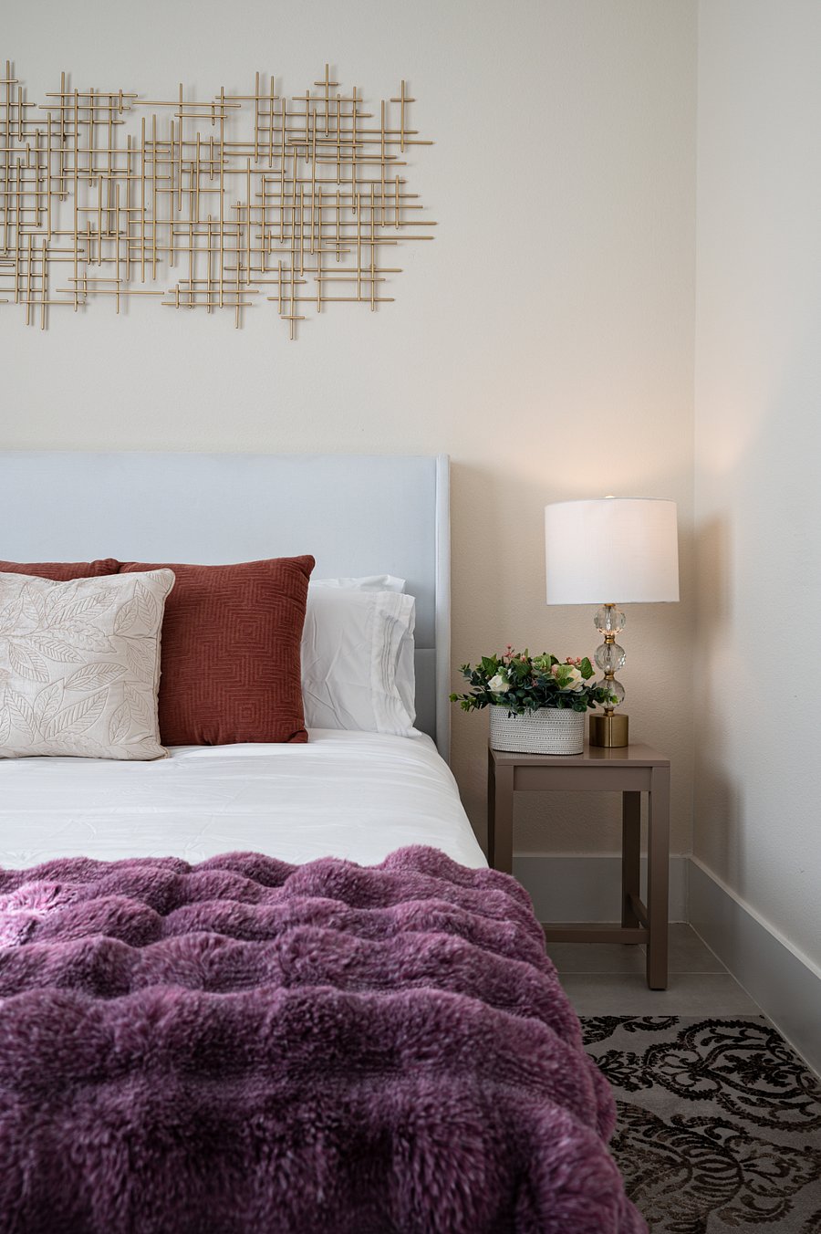 A cozy bedroom with a queen size plush bed, a large window with blackout curtains, touch of greenery.