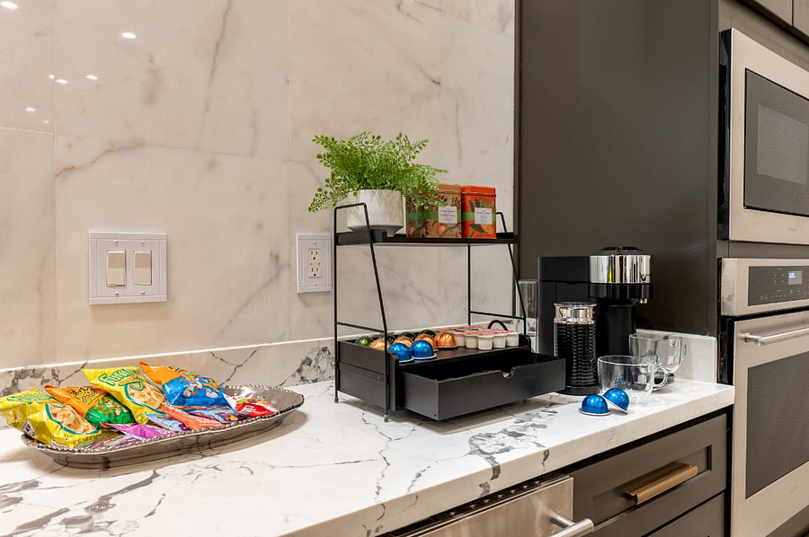 A kitchen counter with a coffee maker, a complimentary snack tray and coffee&tea. 