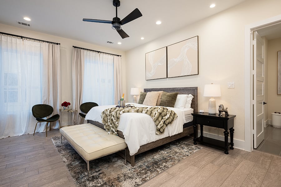 A spacious bedroom with a king-size bed, a ceiling fan, and large windows.