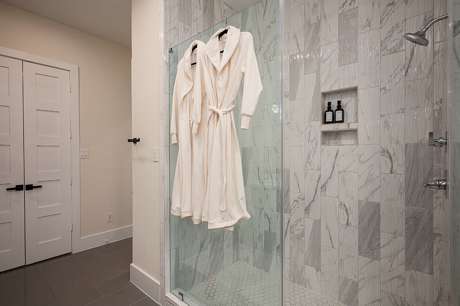 A luxurious bathroom with a glass shower, marble tile, and plush robes. 