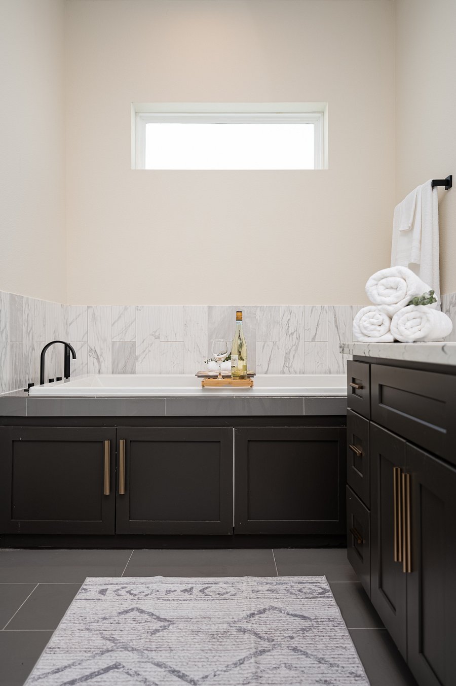 A bathroom with dark cabinets and a patterned rug. 