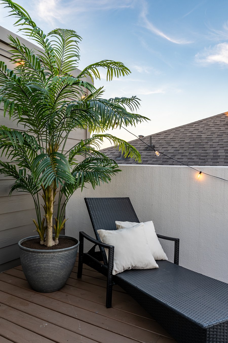 A cozy and relaxing outdoor space with a lounge chair, a potted plant, and string lights. 