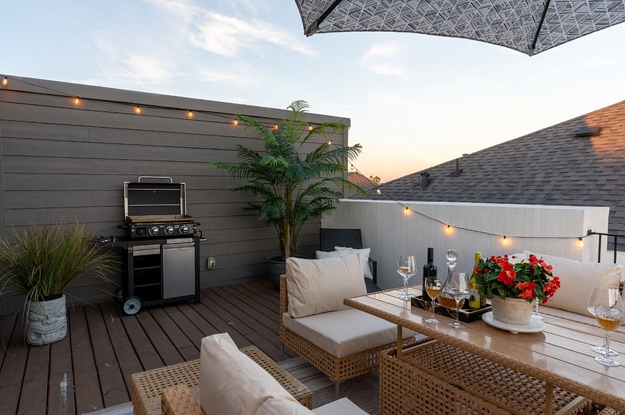 A rooftop patio with a grill, a table and chairs, and string lights. 