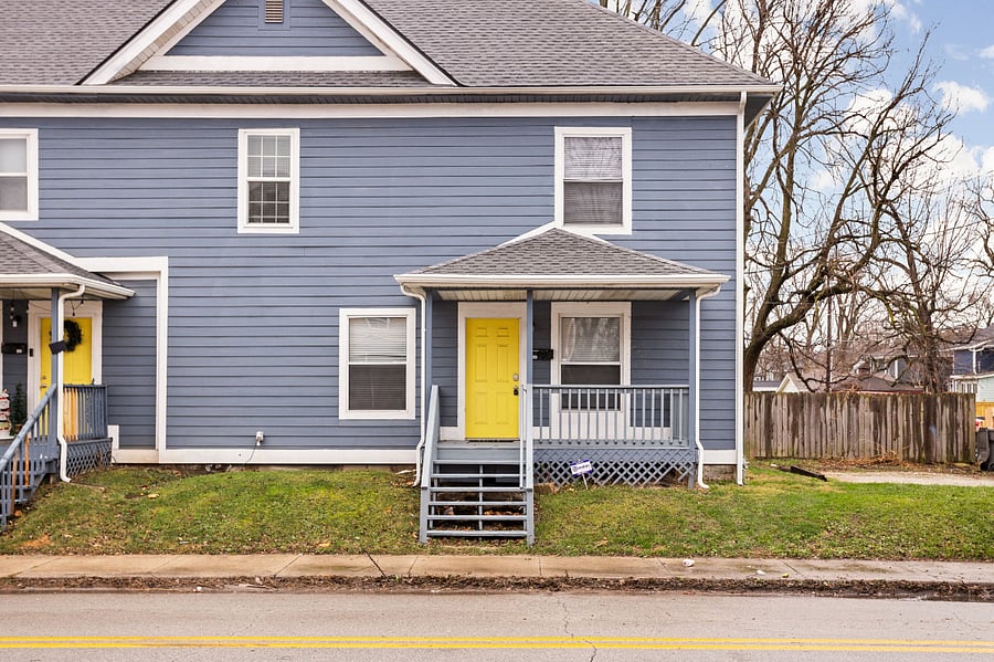 It is a charming blue home with a bright yellow door and a cozy front porch.