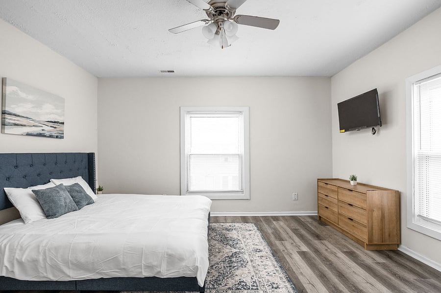 Modern and cozy bedroom with a stylish design, featuring a plush blue headboard, sleek wooden furniture, and ample natural light.
