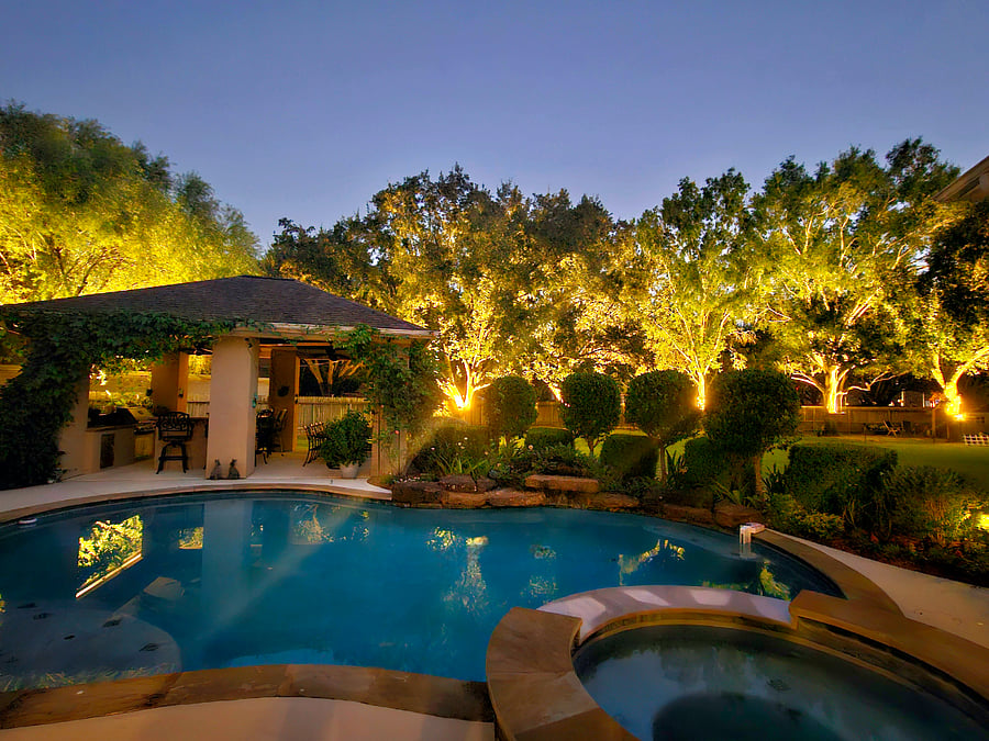 As evening falls, the beautifully illuminated trees transform the poolside into a dreamy, resort-style retreat.