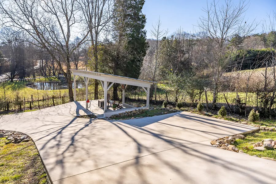 Driveway leads down to another covered seating area and pond
