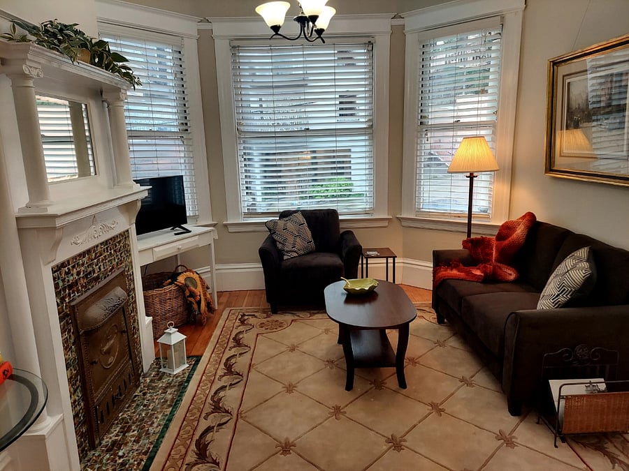 Living room with bay windows. No fires allowed in fireplace. All original 1907 architectural details. Smart TV, sofa, armchair, coffee table, basket with blankets