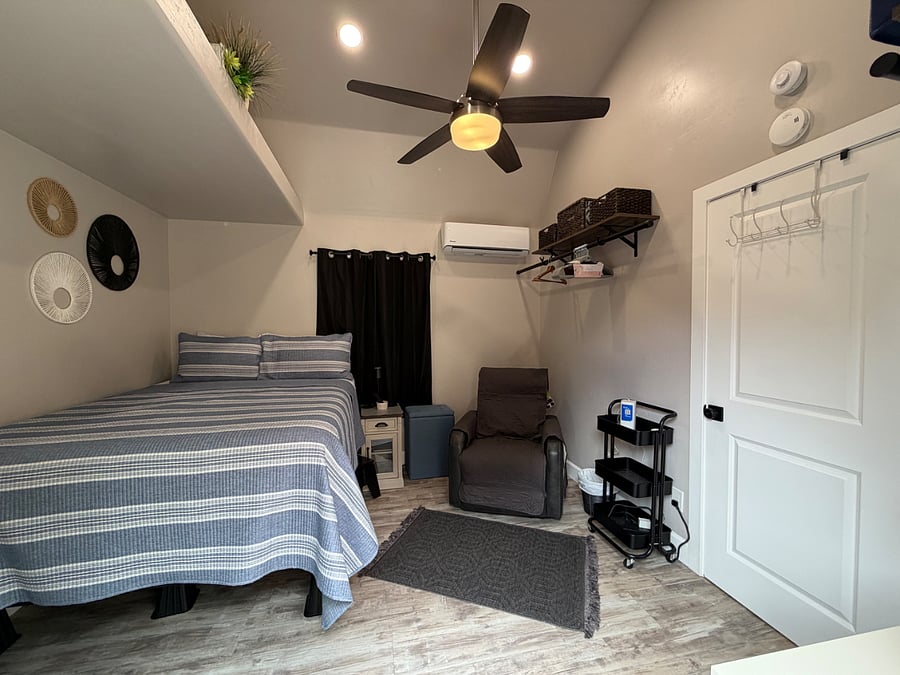 Bedroom with mini-split AC/Heat pump (very quiet) queen-size bed, smart TV, including e-recliner, e-night stand, shelving with hanging rods for clothing and sliding glass door to exterior. 
