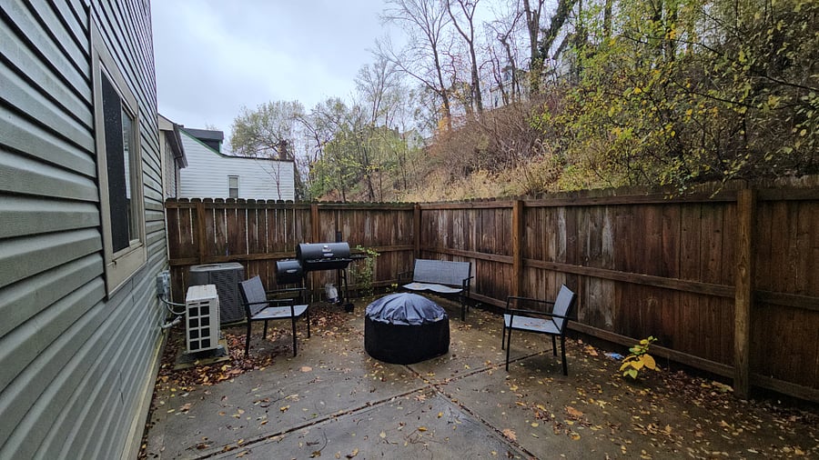 Fenced backyard with grill (charcoal and wood fire), fire pit, and outdoor sits.