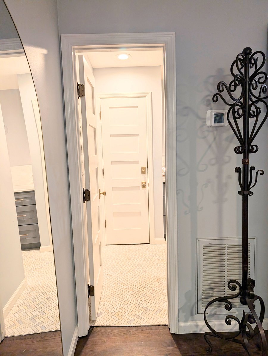Door leading into newly remodeled bathroom with marble tiles and brass fixtures. 