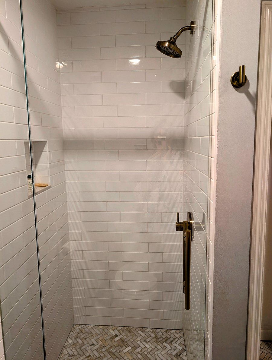 Lovely marble tiled shower with brass fixtures and glass shower door.