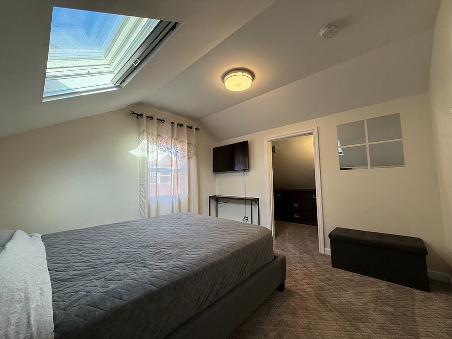 Relaxing bedroom with a comfy queen-size bed, wall-mounted smart TV, and generous walk-in closet.