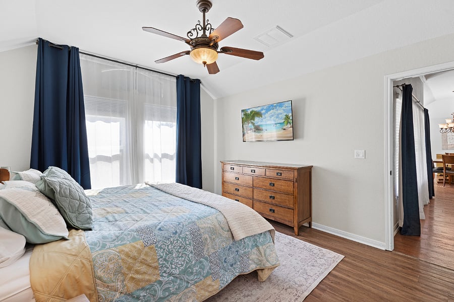 Master bedroom has blackout window shades, wall-mounted smart TV, nightstands with bedside lamps, and dresser.