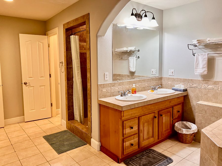Large bathroom with double vanity, walk-in shower, separate toilet room, large soaking bath tub, and sauna. 