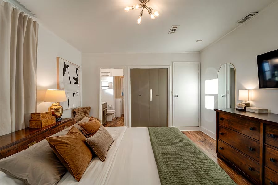 View of the primary bedroom into the en suite bathroom and laundry area with full size washer and dryer. A closet and large dresser provide ample clothing storage.