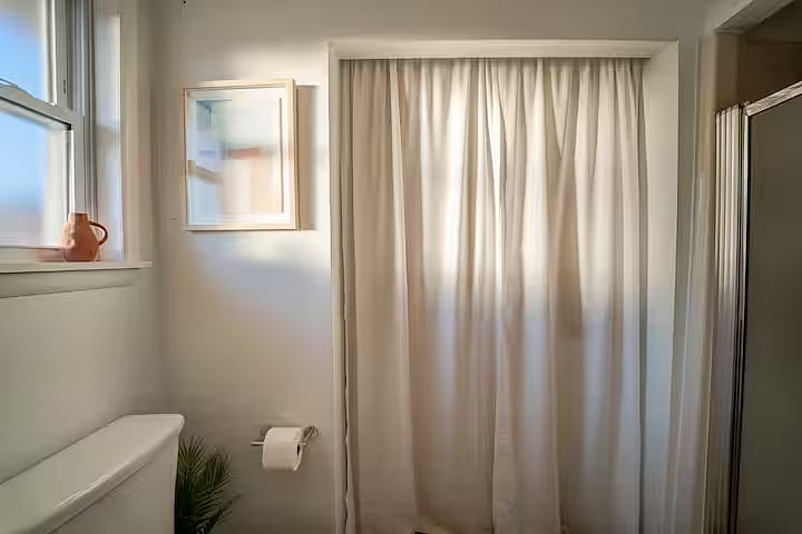 Laundry area located in the primary bedroom's bathroom, with curtains to conceal the full-size washer and dryer and all you need to clean clothing.