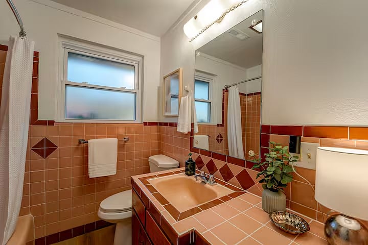 An historical rare design gem!! Mid-century pink tiled bathroom, vanity with sink, shower/tub, mirror, and light fixture are all original. The adjustable shower head is new.