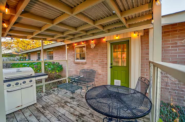 Covered pack porch with grill, comfortable vintage furniture including dining table, chairs, and gliding bench. The string lights automatically come on at dusk.