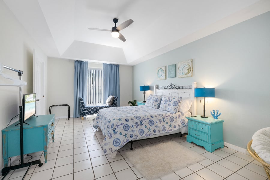 Primary bedroom with queen bed, charger pads, lamps, side tables, dresser, smart TV, clothing rack, and 2 seating areas.