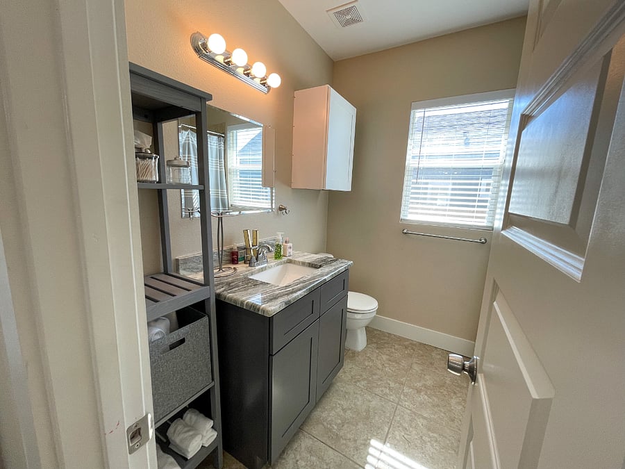 Guest bathroom featuring single vanity, open shelving and shower/tub combo.