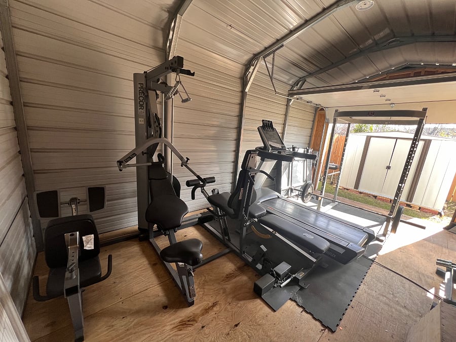 Fully furnished home gym in large storage shed. Treadmill, squat rack, barbell, dumbbells, bumper plates, pulley system, and step-up included.