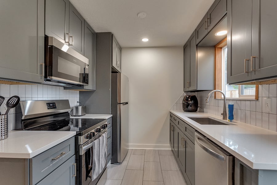 Updated kitchen with all stainless steel appliances, dishwasher, stone tile floors, and view of fenced and gated backyard