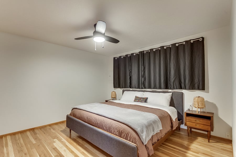 Master bedroom with a king size bed and bedside tables as well as ceiling fan and blackout curtains