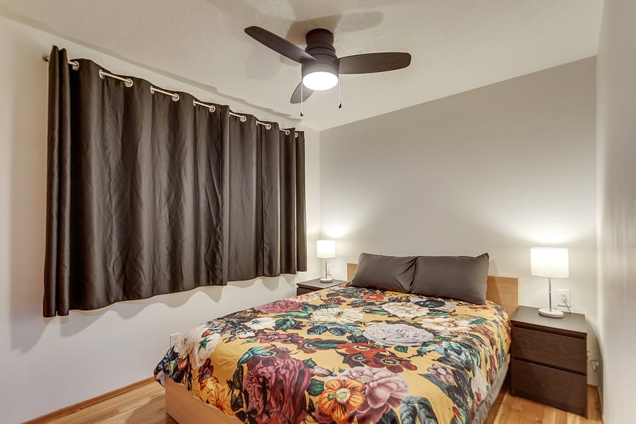 Spare bedroom with queen size bed and bedside tables as well as ceiling fan and blackout curtains