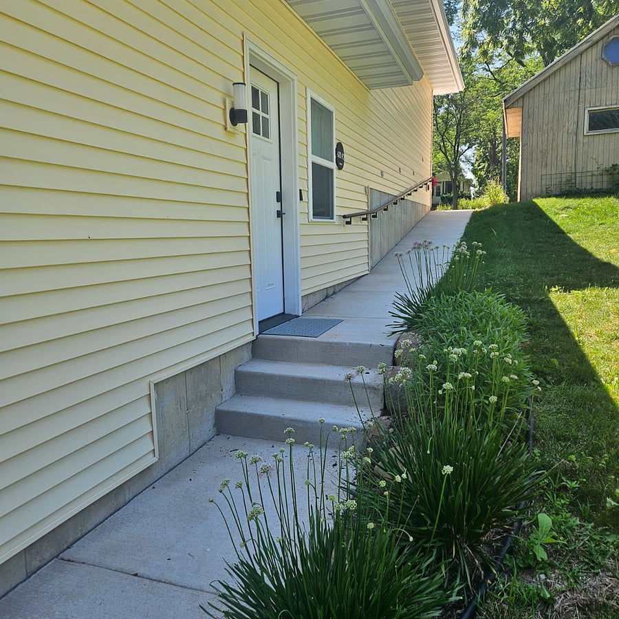 View from alleyway. Sidewalk with handrail leading to front door of apartment.