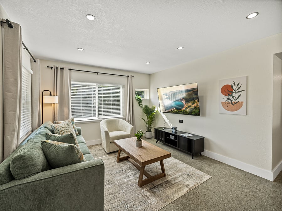 This modern living room features earth-toned decor, large windows for natural light, and cozy seating, including a swivel chair. A 65" TV is perfect for movie nights, while natural materials and soft lighting create a serene, inviting atmosphere.