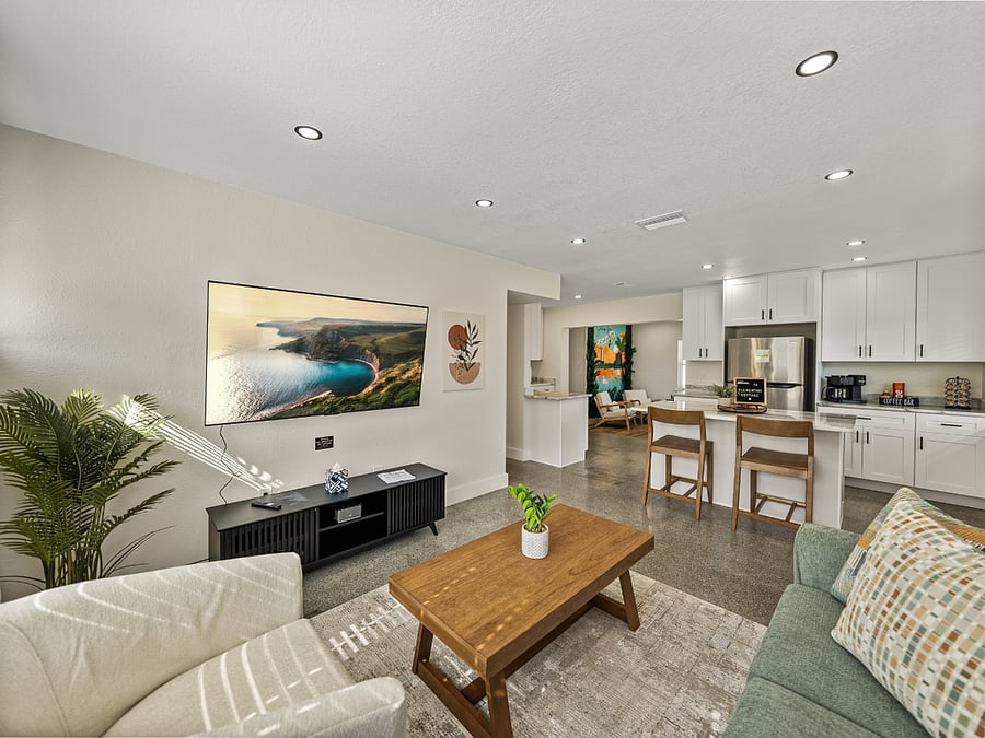This modern living room features earth-toned decor, large windows for natural light, and cozy seating, including a swivel chair. A 65" TV is perfect for movie nights, while natural materials and soft lighting create a serene, inviting atmosphere.