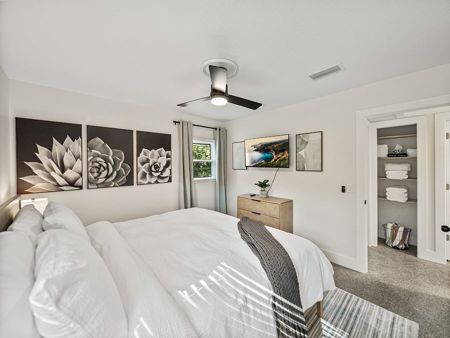 Spacious master bedroom with a king bed, warm earth-tone decor, and dual windows for natural light. Enjoy a mounted TV, blackout curtains, ceiling fan, and two closetsperfect for comfort and longer stays.