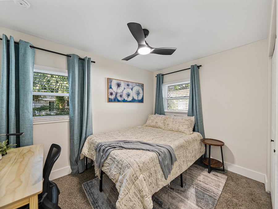Spacious third bedroom with a queen bed, terrazzo floors, and natural light. Includes a desk, mounted TV, blackout curtains, and a full-length mirror in the roomy closetideal for work or rest.