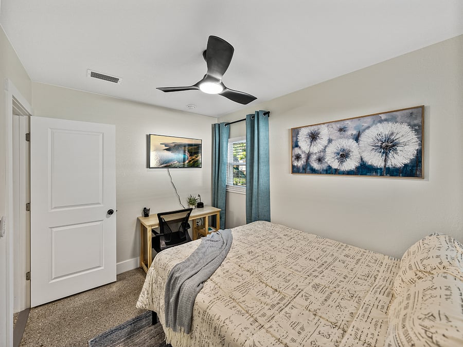 Spacious third bedroom with a queen bed, terrazzo floors, and natural light. Includes a desk, mounted TV, blackout curtains, and a full-length mirror in the roomy closetideal for work or rest.