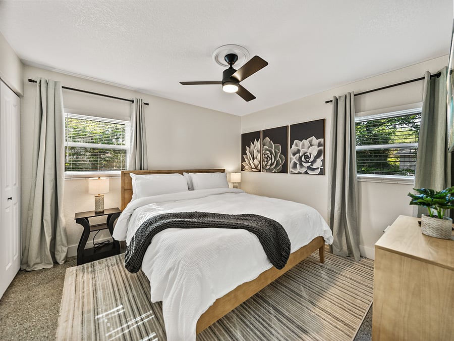 Spacious master bedroom with a king bed, warm earth-tone decor, and dual windows for natural light. Enjoy a mounted TV, blackout curtains, ceiling fan, and two closetsperfect for comfort and longer stays.