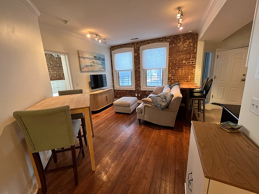 View from entry. High-top solid wood table with two barstools. Storage cabinet with shelves.