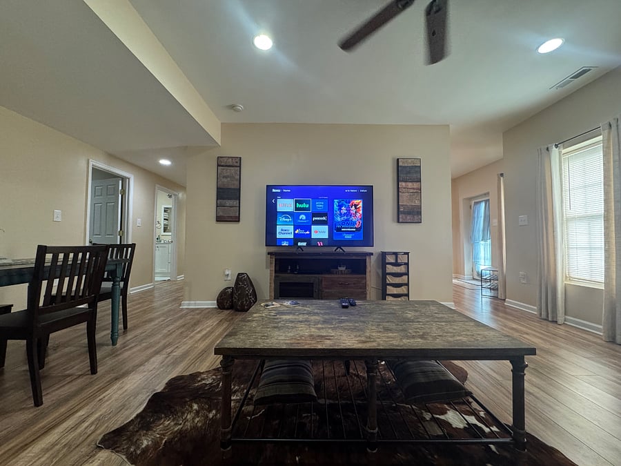 Living room and dining area combo (view 2); While seated on couch (view 2); 70" 4k smart TV with 4k Roku device and DVD player; hallway to right leads back toward front door and foyer; hallway to left leads to bedroom #1, bathroom and kitchen