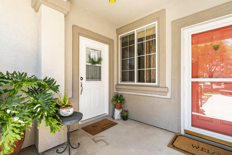 Entrance has white door and welcome sign on wall with lights for arriving at night.