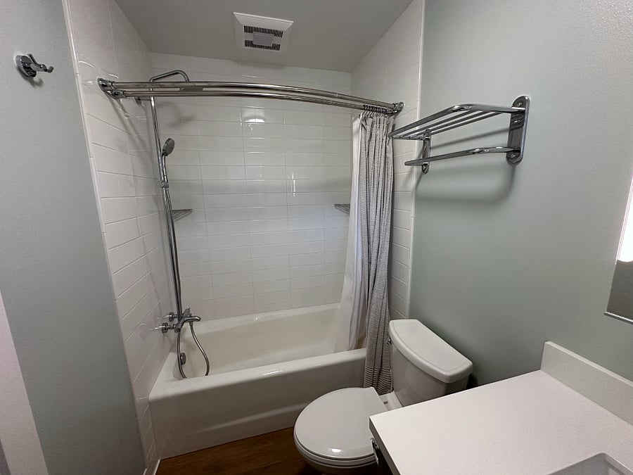 Tiled shower with cast-iron tub, rain head with hand sprayer, lighted mirror, and radiant cove heater.