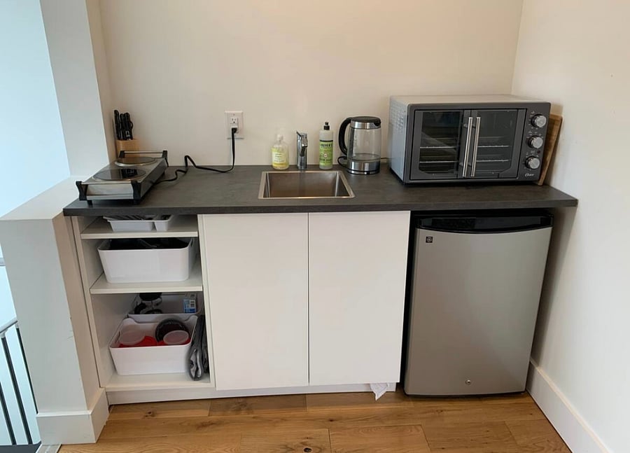 Kitchenette with stove-plates, toaster oven, fridge, sink, and cleaning supplies.
