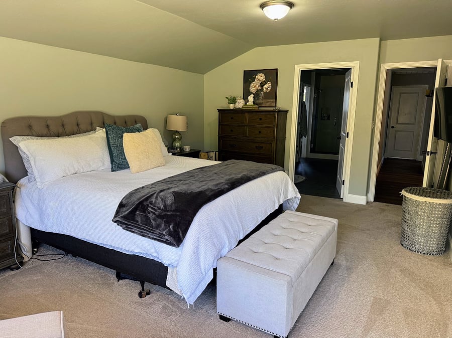 Primary bedroom includes storage ottoman, dresser, and large nightstands.