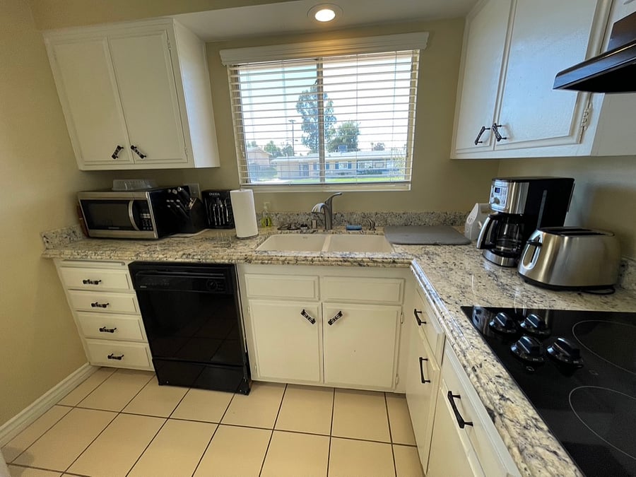 Granite countertops match a granite breakfast bar. The dishwasher, microwave, coffee maker, hand-held electric mixer supplement an electric range and full-size refrigerator.