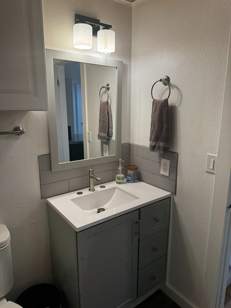 Bathroom sink space, with storage, hair dryer, soap dispenser and storage container, granite countertop and tile backsplash.