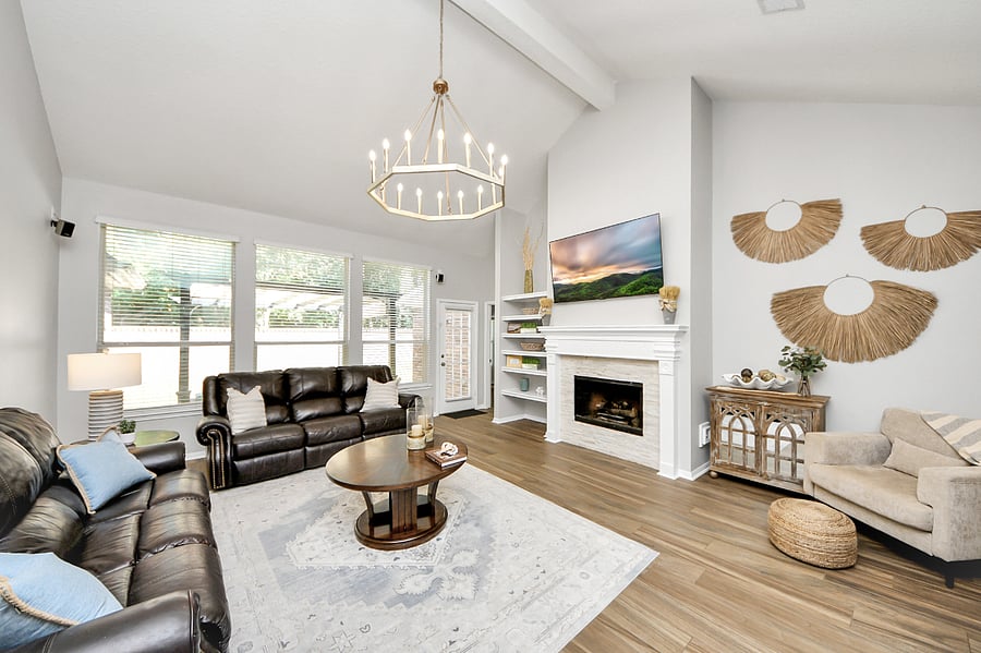Spacious living room with high ceiling, updated light fixture, and wall of windows. Plenty of sitting spaces with 2 large couches, a chair and 2 barstools.