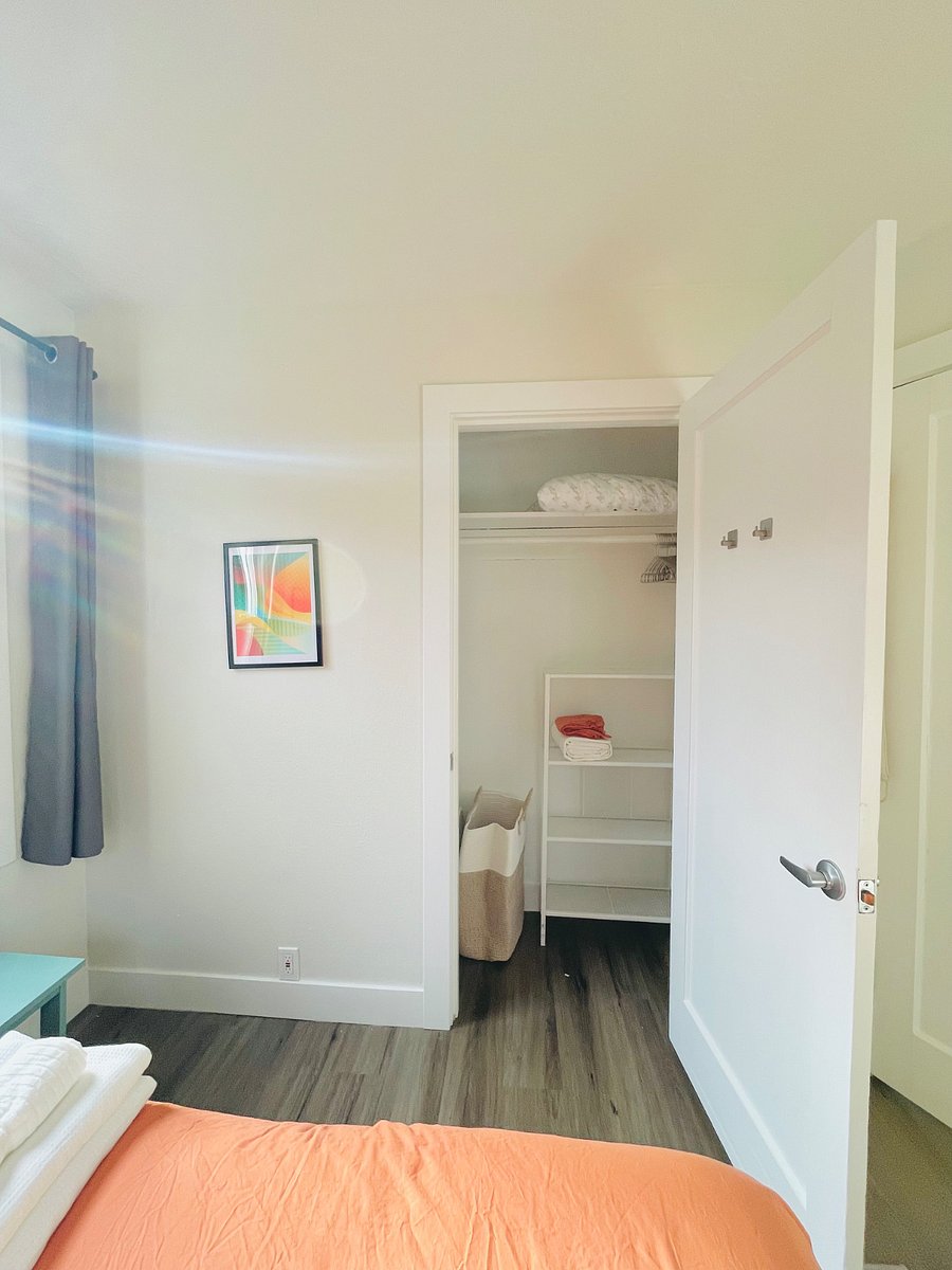 Standard closet in room, with laundry hamper, door hooks, hangers, extra bedding