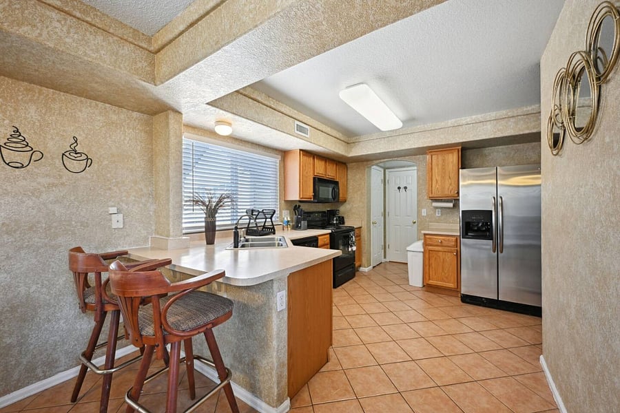 View into the kitchen. To the left of the full-size fridge and freezer two doors; one is a broom closet, and the other is a half bathroom. 