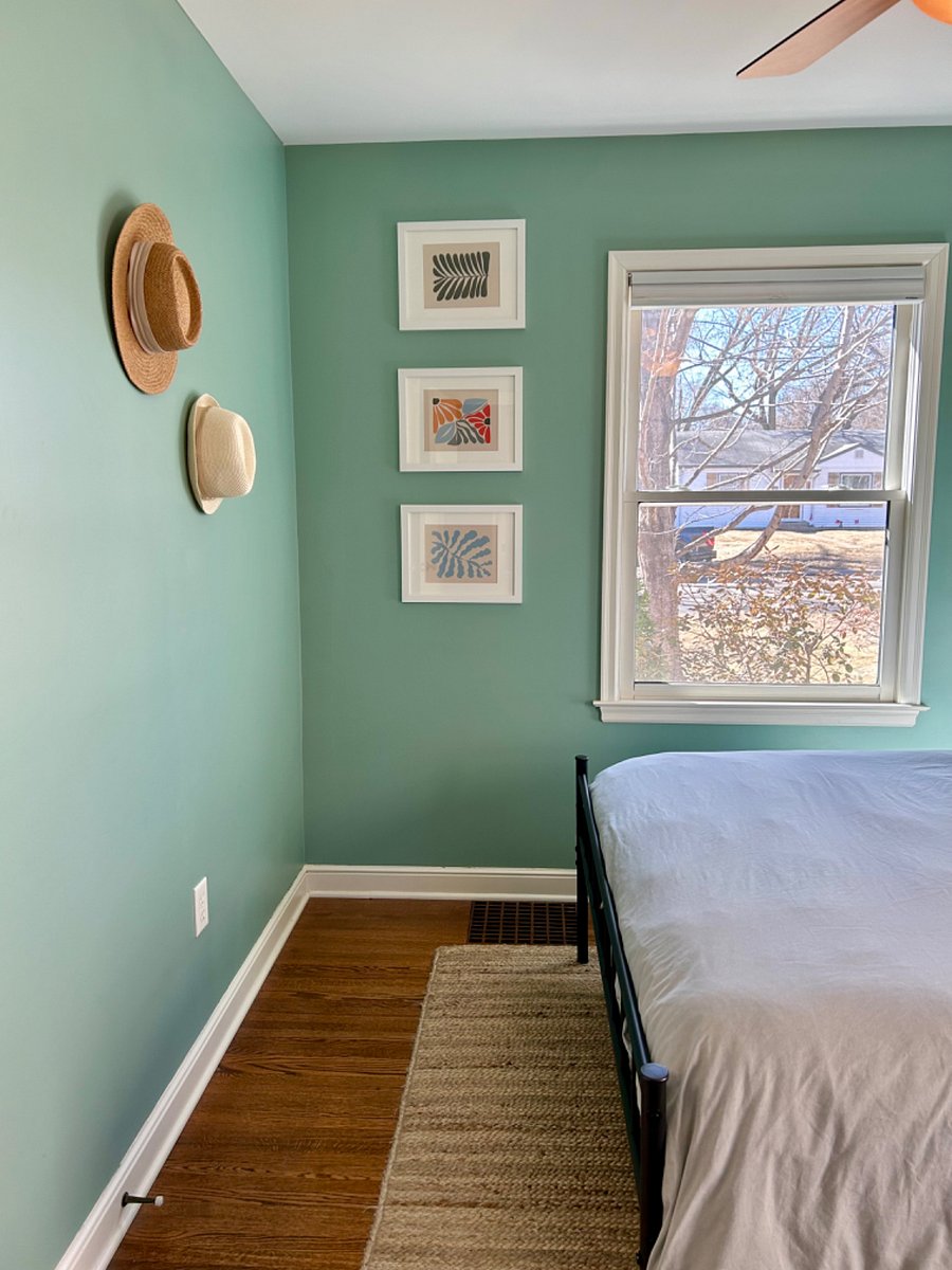 Main floor bedroom 2 features a queen size bed, desk and chair, nightstand, lamp, closet with a laundry basket and hangers.