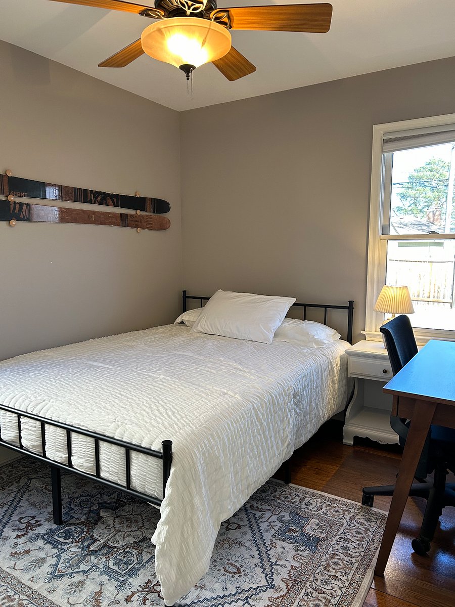 Main floor bedroom 1 features a queen size bed, desk and chair, nightstand, lamp, closet with a laundry basket and hangers.